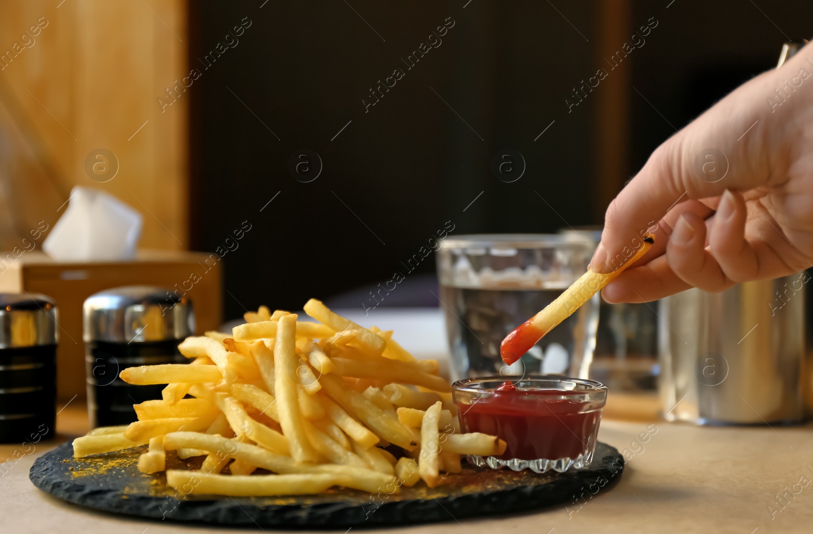 Photo of Woman dipping French fries into red sauce in cafe, closeup