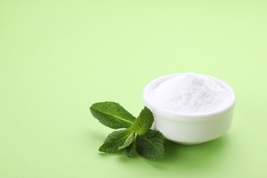 Photo of Bowl of sweet powdered fructose and mint leaves on light green background. Space for text