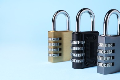 Steel combination padlocks on light blue background, closeup. Space for text