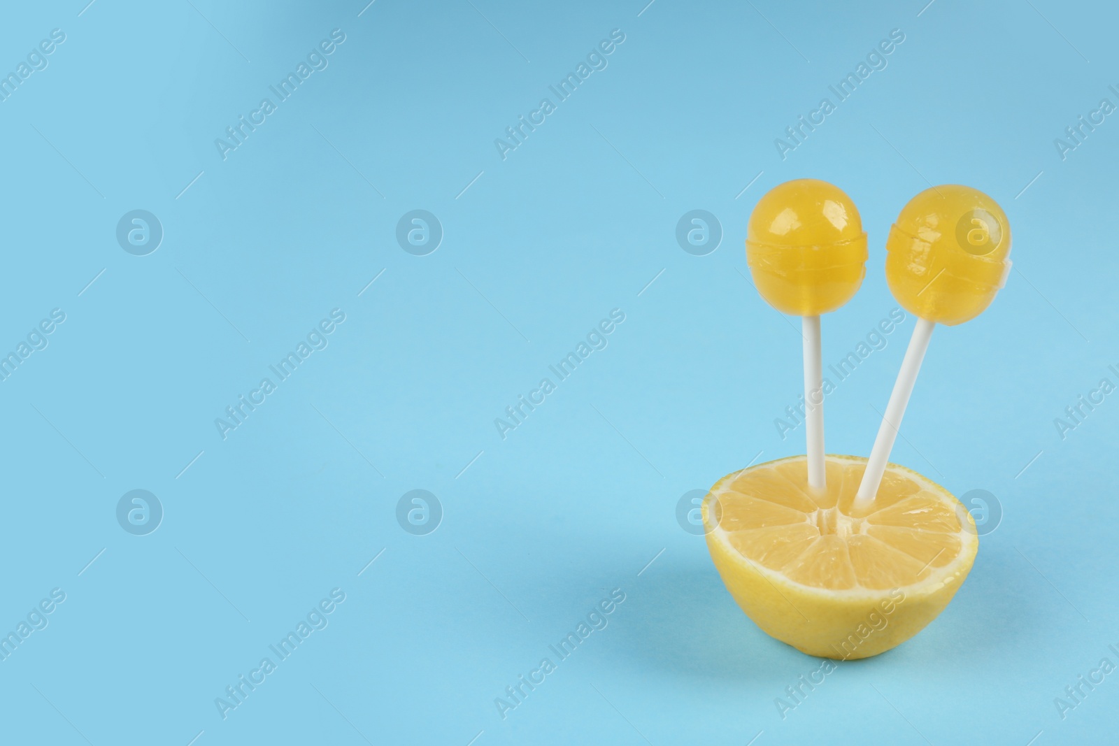 Photo of Fresh lemon with yellow lollipops on light blue background