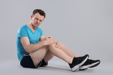 Man suffering from leg pain on grey background