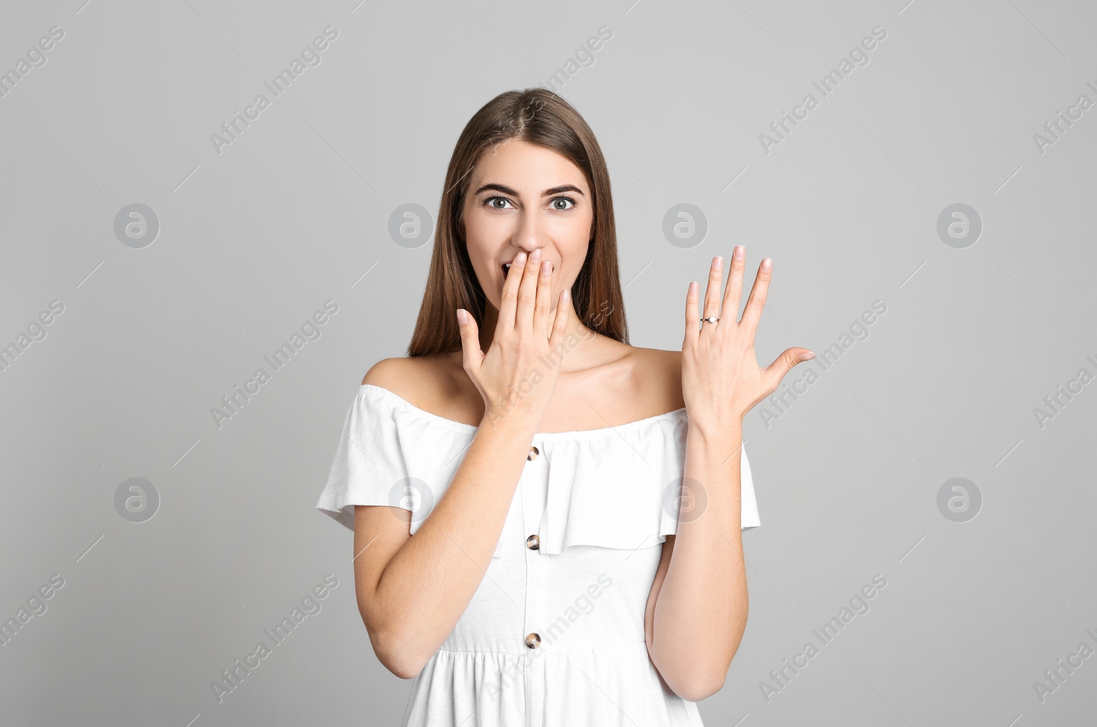 Photo of Emotional young woman wearing beautiful engagement ring on grey background