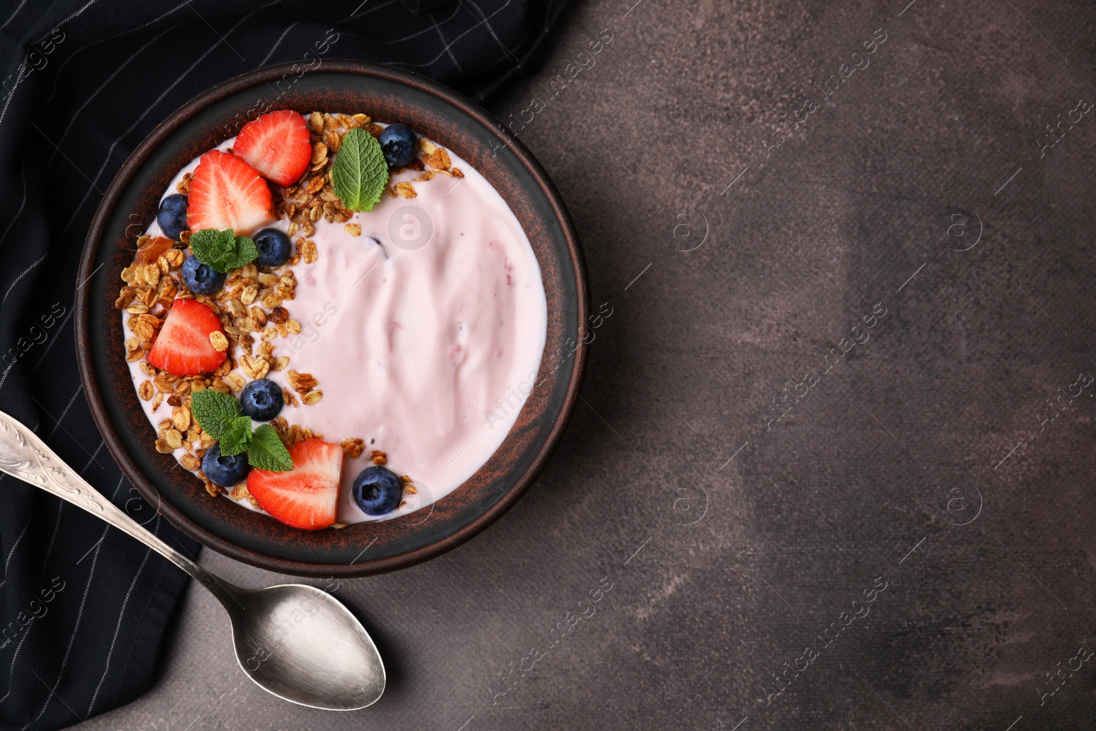 Photo of Bowl with yogurt, berries and granola on brown table, flat lay. Space for text