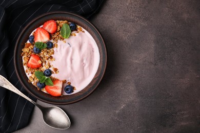 Photo of Bowl with yogurt, berries and granola on brown table, flat lay. Space for text