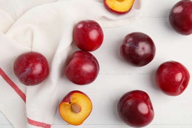 Delicious ripe plums on white wooden table, flat lay