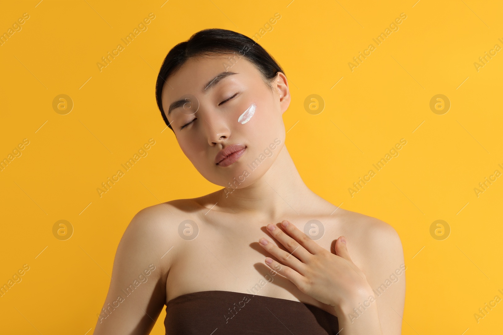 Photo of Beautiful young woman with sun protection cream on her face against orange background