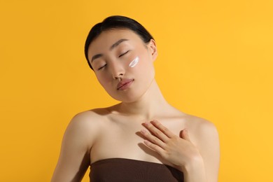 Beautiful young woman with sun protection cream on her face against orange background