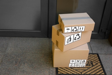 Photo of Cardboard boxes with different packaging symbols on door mat near entrance, space for text. Parcel delivery