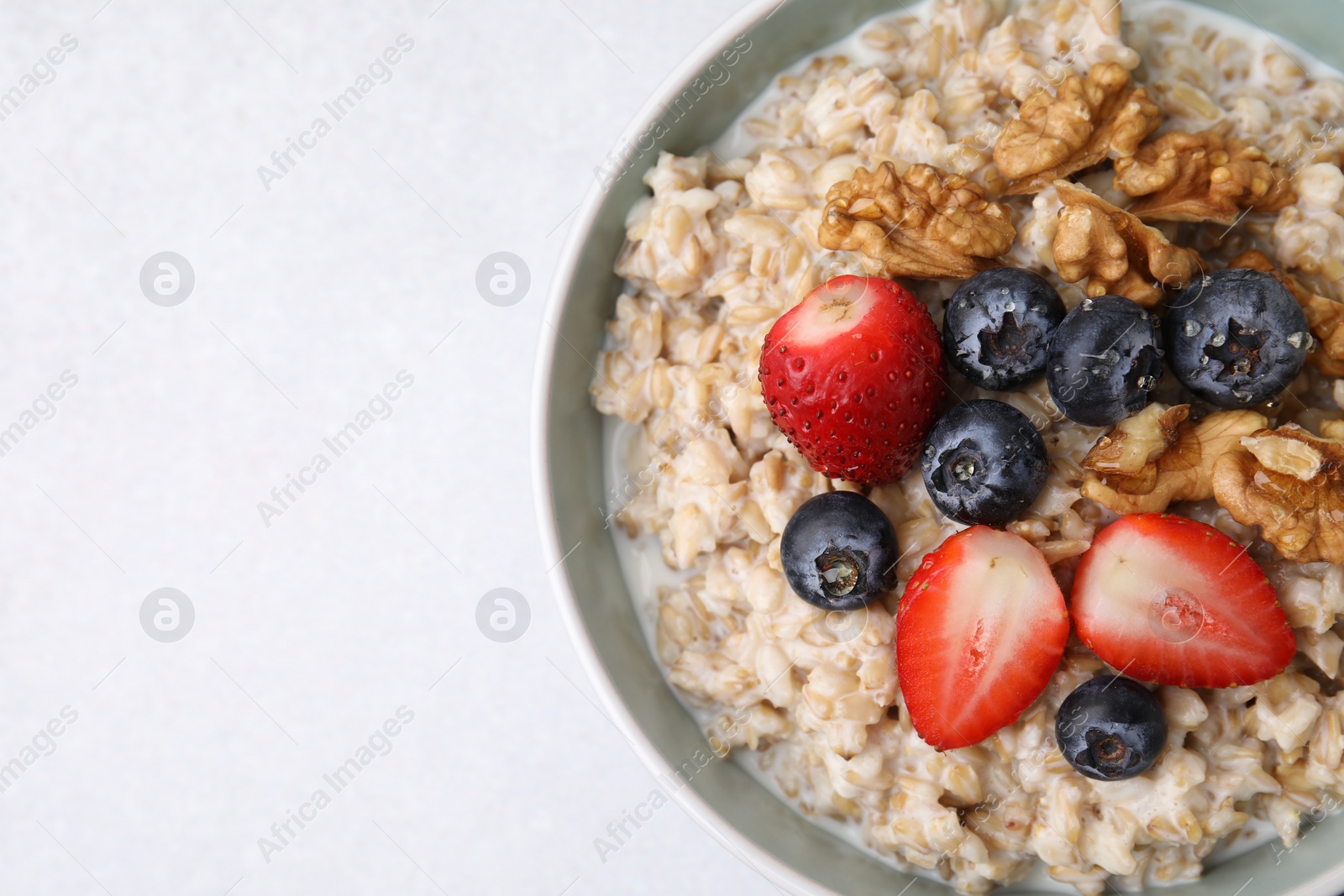 Photo of Tasty oatmeal with strawberries, blueberries and walnuts in bowl on grey table, top view. Space for text