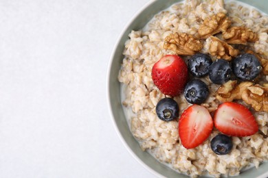 Photo of Tasty oatmeal with strawberries, blueberries and walnuts in bowl on grey table, top view. Space for text