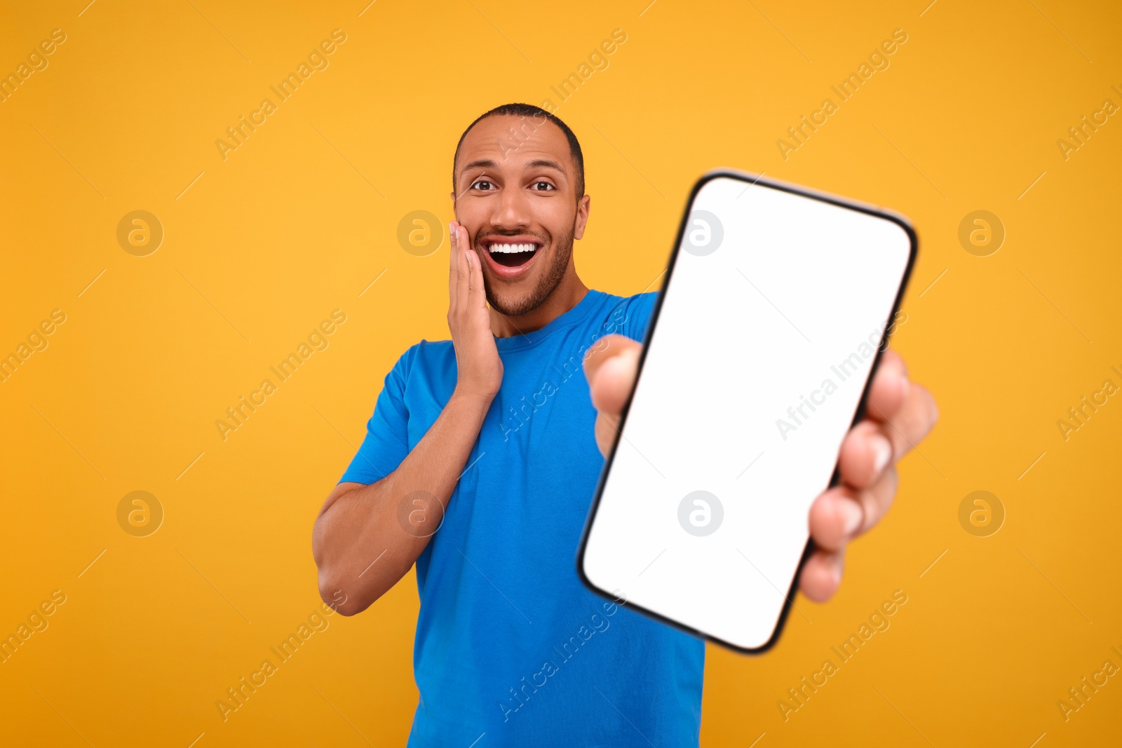 Photo of Surprised man showing smartphone in hand on yellow background