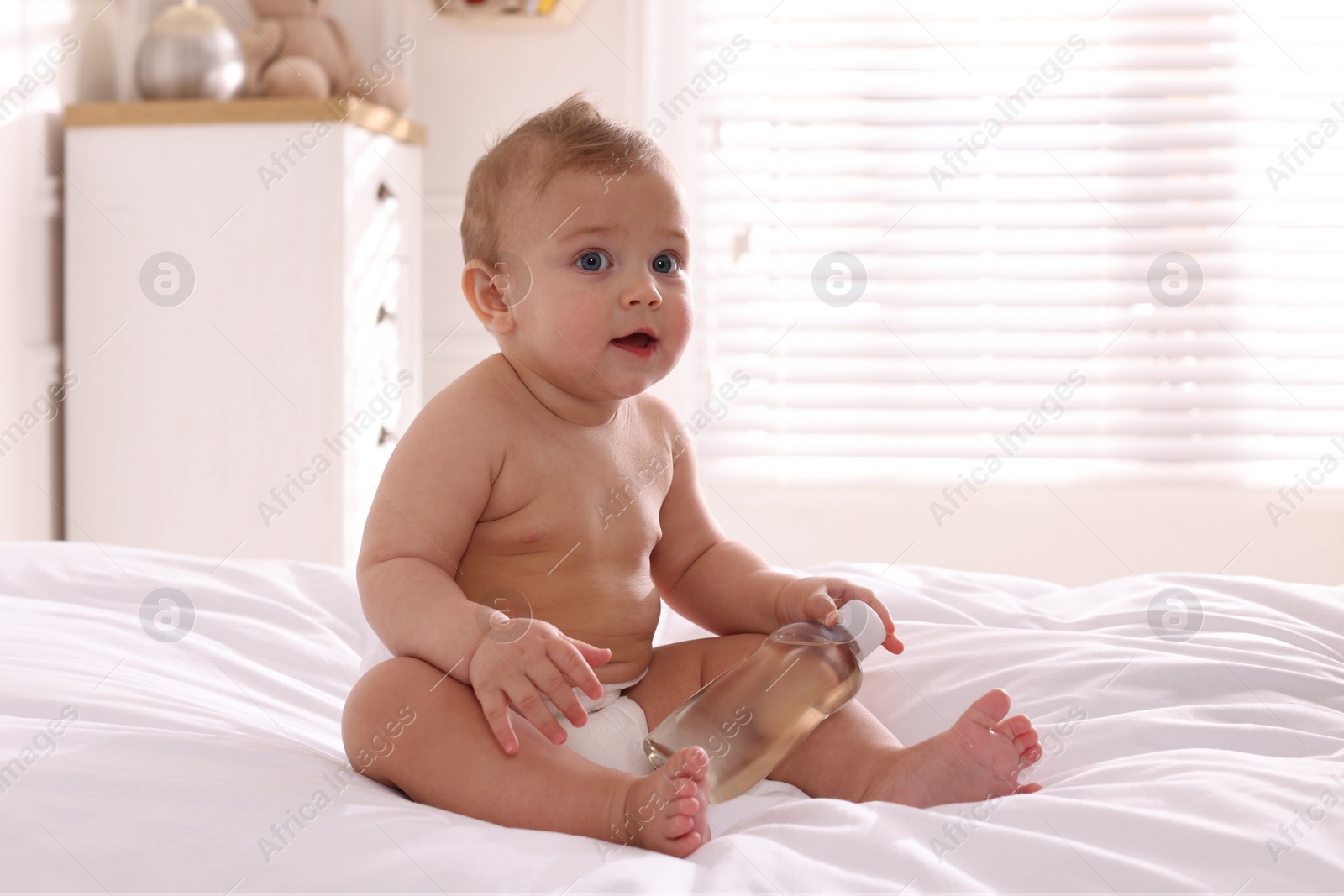 Photo of Cute little baby with bottle of massage oil on bed at home