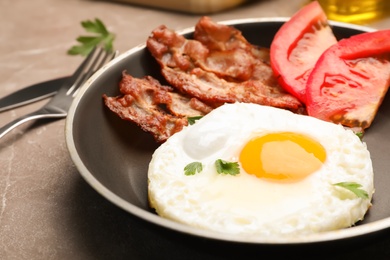 Photo of Pan with fried sunny side up egg, bacon and tomato on table, closeup