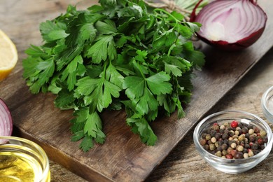 Board with fresh parsley, peppercorns and other products on wooden table, closeup