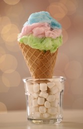 Photo of Sweet cotton candy in waffle cone on table against blurred lights, closeup