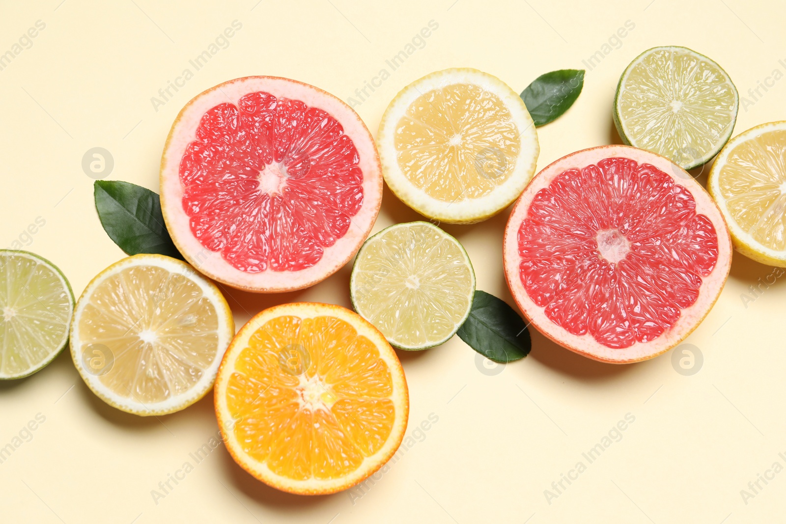 Photo of Different cut citrus fruits and leaves on beige table, flat lay