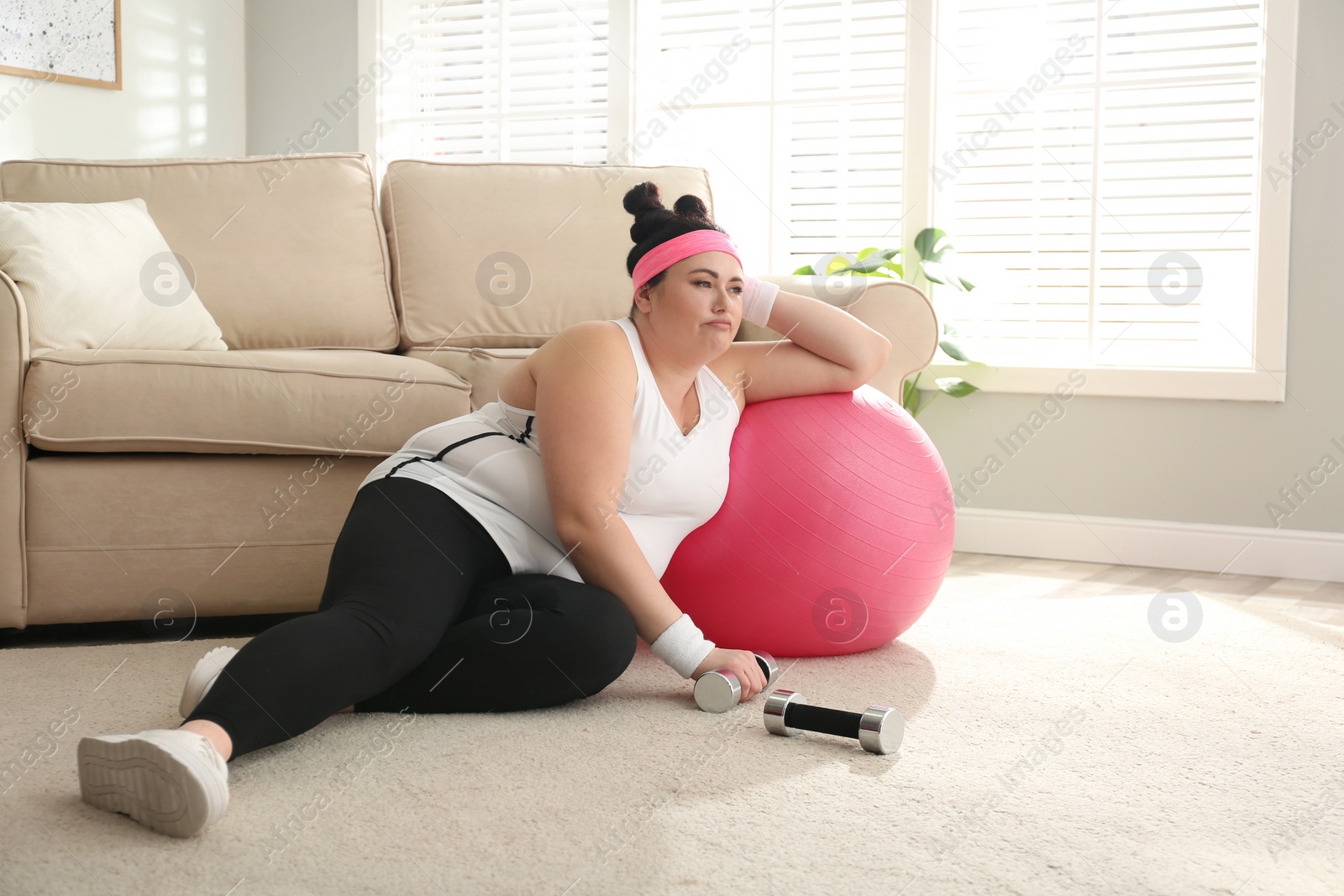 Photo of Lazy overweight woman with sport equipment on floor at home