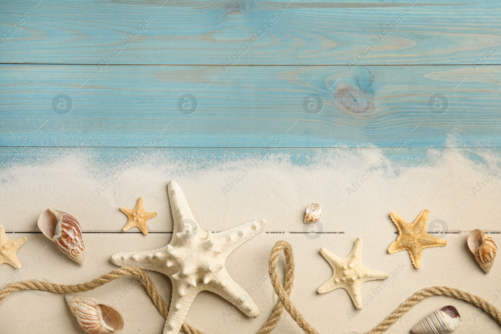 Photo of Beautiful sea stars, shells, rope and sand on blue wooden background, flat lay. Space for text