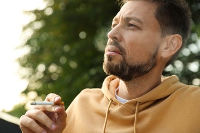 Handsome mature man smoking cigarette outdoors on sunny day