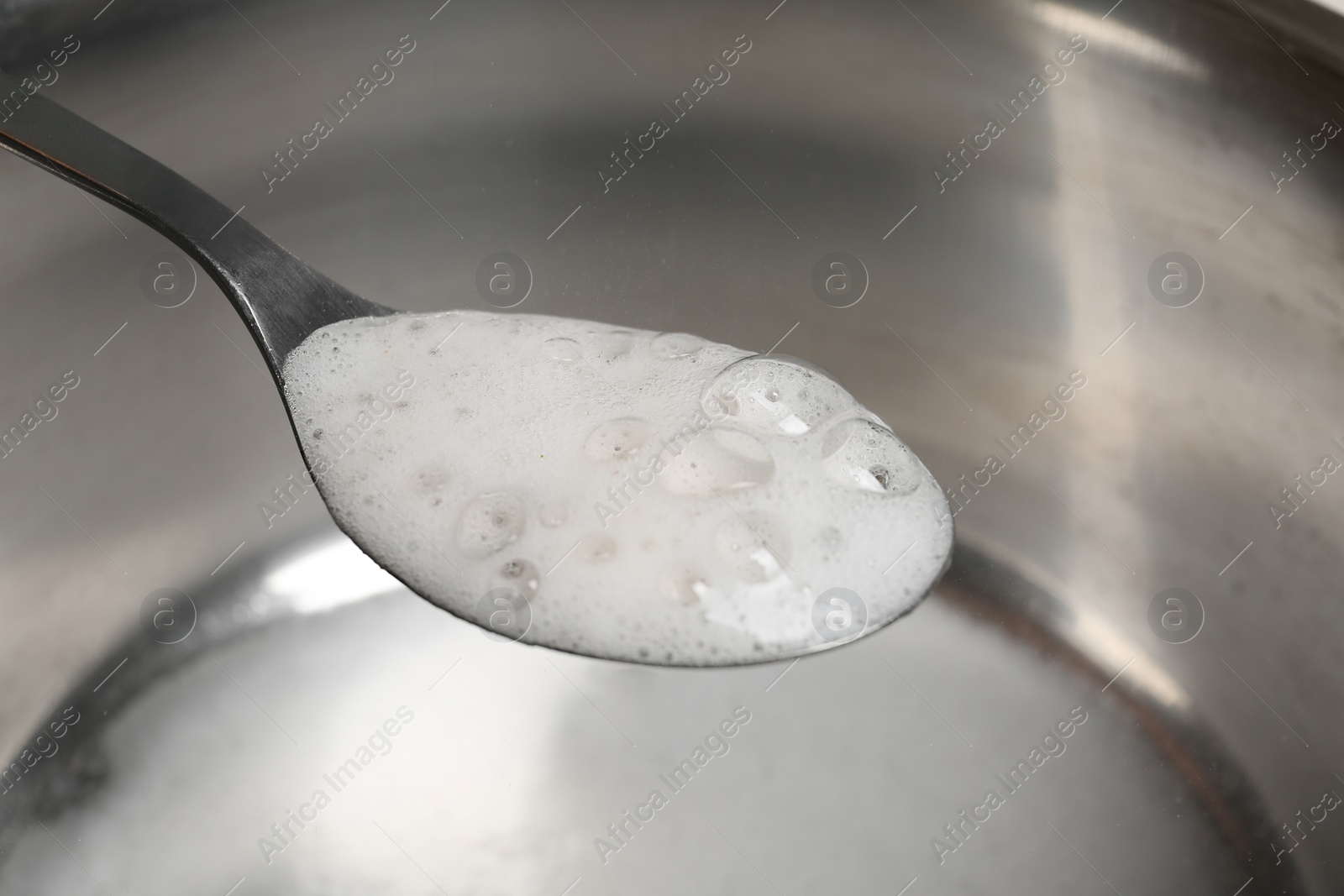 Photo of Chemical reaction of vinegar and baking soda in spoon over saucepan, closeup