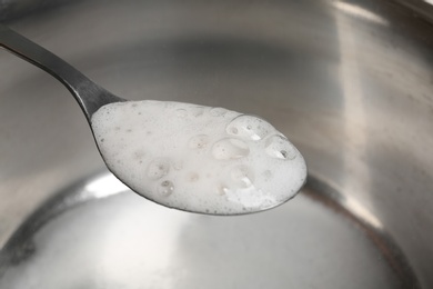 Photo of Chemical reaction of vinegar and baking soda in spoon over saucepan, closeup