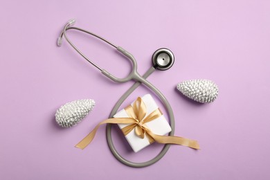 Greeting card for doctor with stethoscope, gift box and Christmas decor on purple background, flat lay