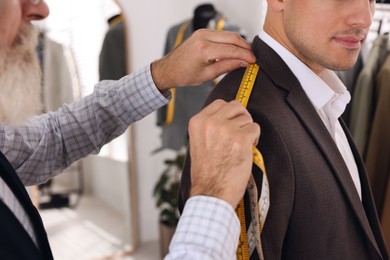 Photo of Professional tailor measuring shoulder seam length on client's jacket in atelier, closeup