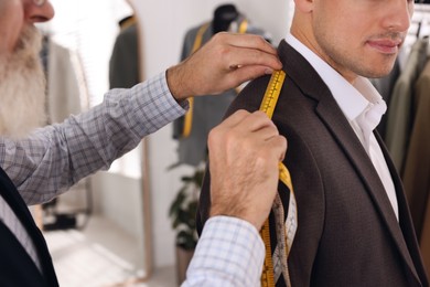 Professional tailor measuring shoulder seam length on client's jacket in atelier, closeup