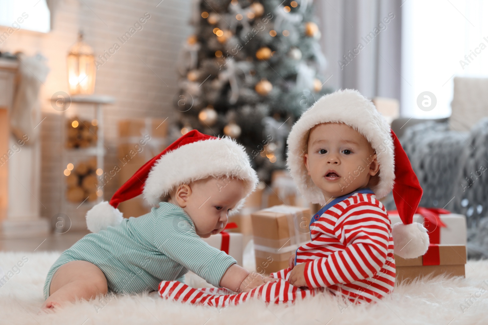 Image of Cute children in Santa hats on floor in room with Christmas tree