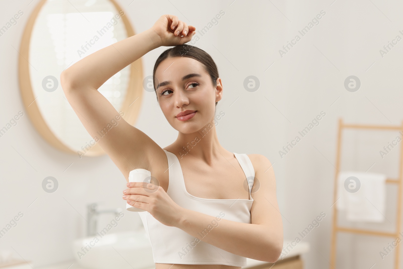 Photo of Beautiful young woman applying deodorant in bathroom