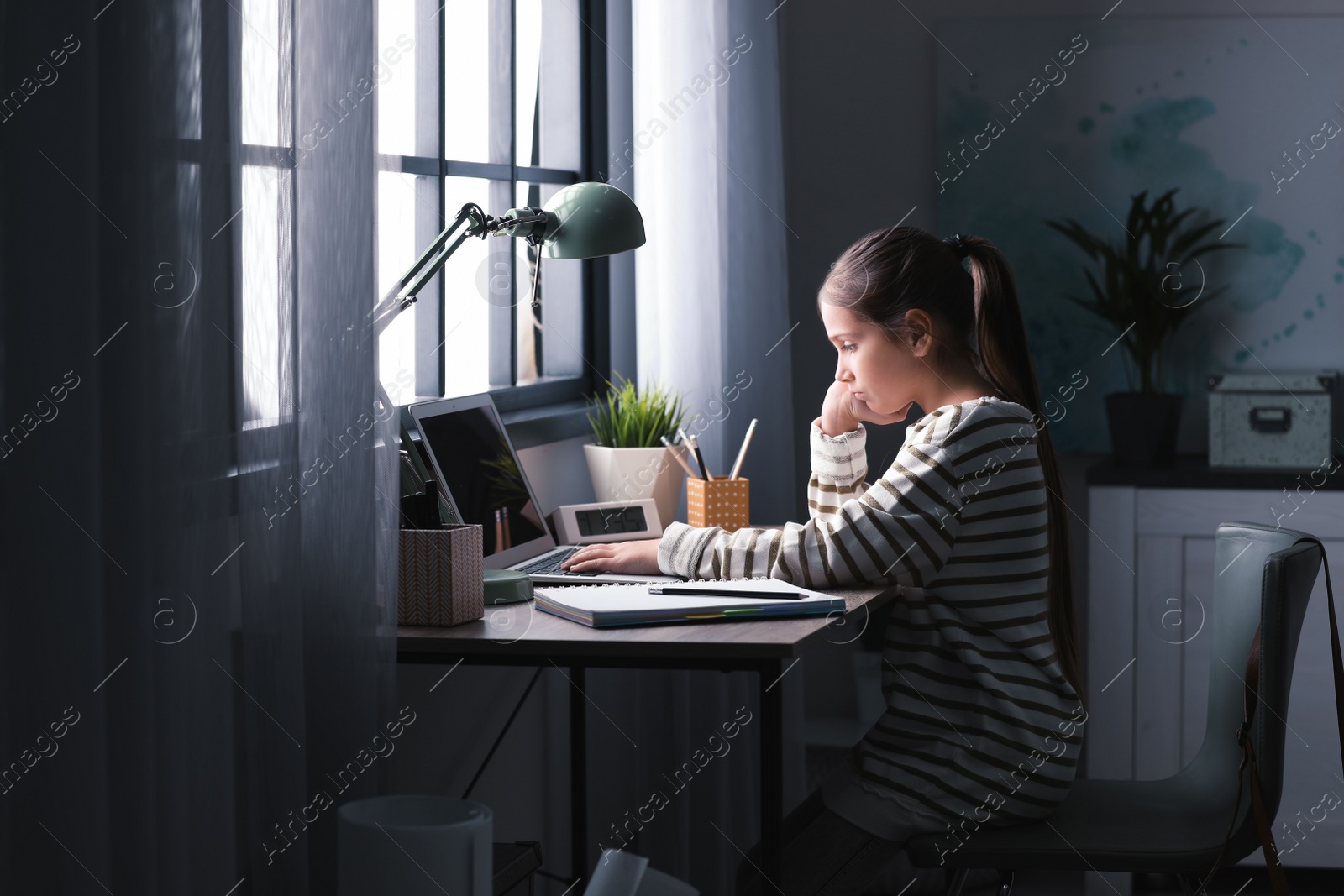 Photo of Pretty preteen girl doing homework at table in room