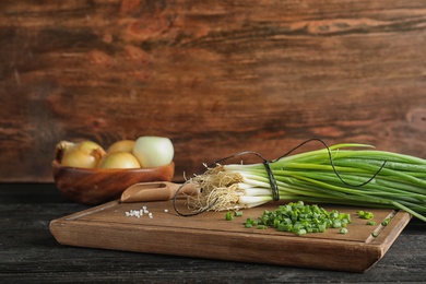 Photo of Board with cut green onion and salt on dark wooden table, space for text