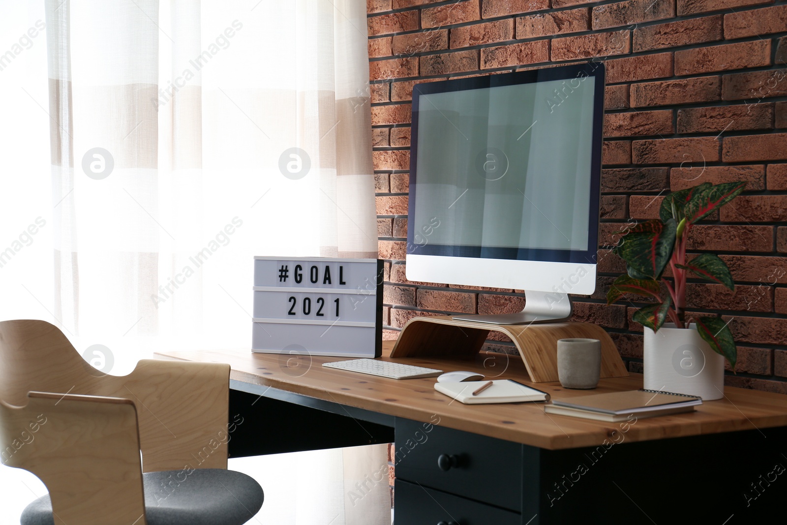 Photo of Light box with hashtag Goal 2021 near computer monitor on wooden desk in office