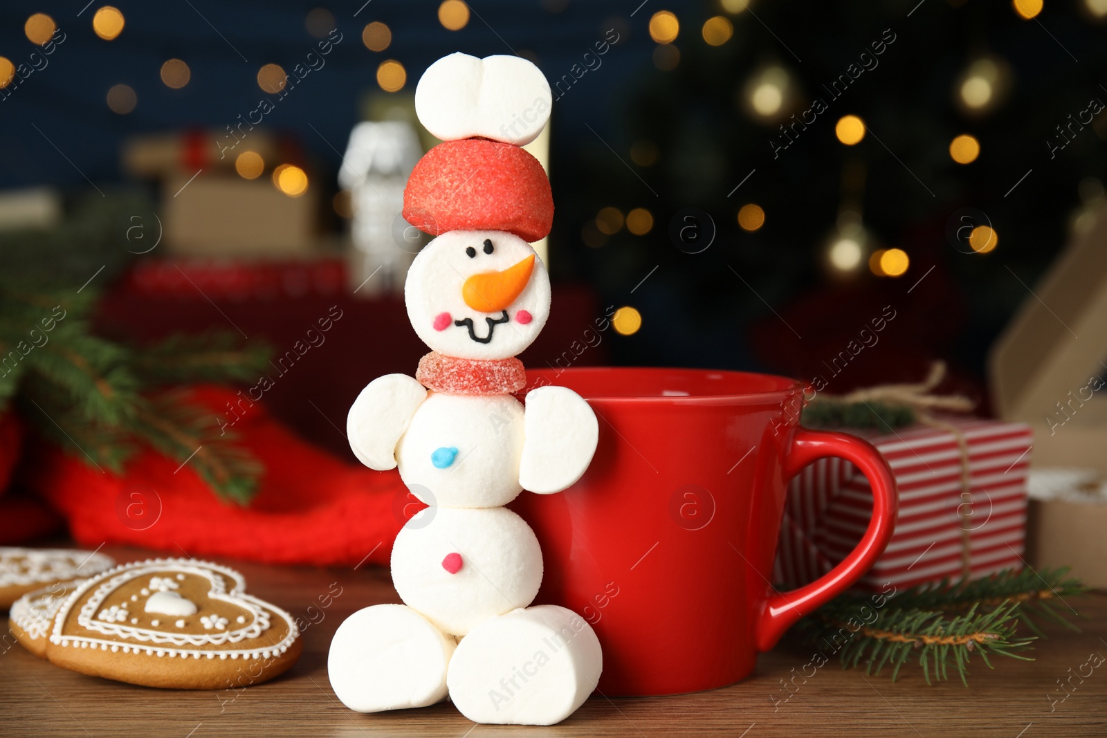 Photo of Funny snowman made of marshmallows on wooden table against blurred lights, closeup