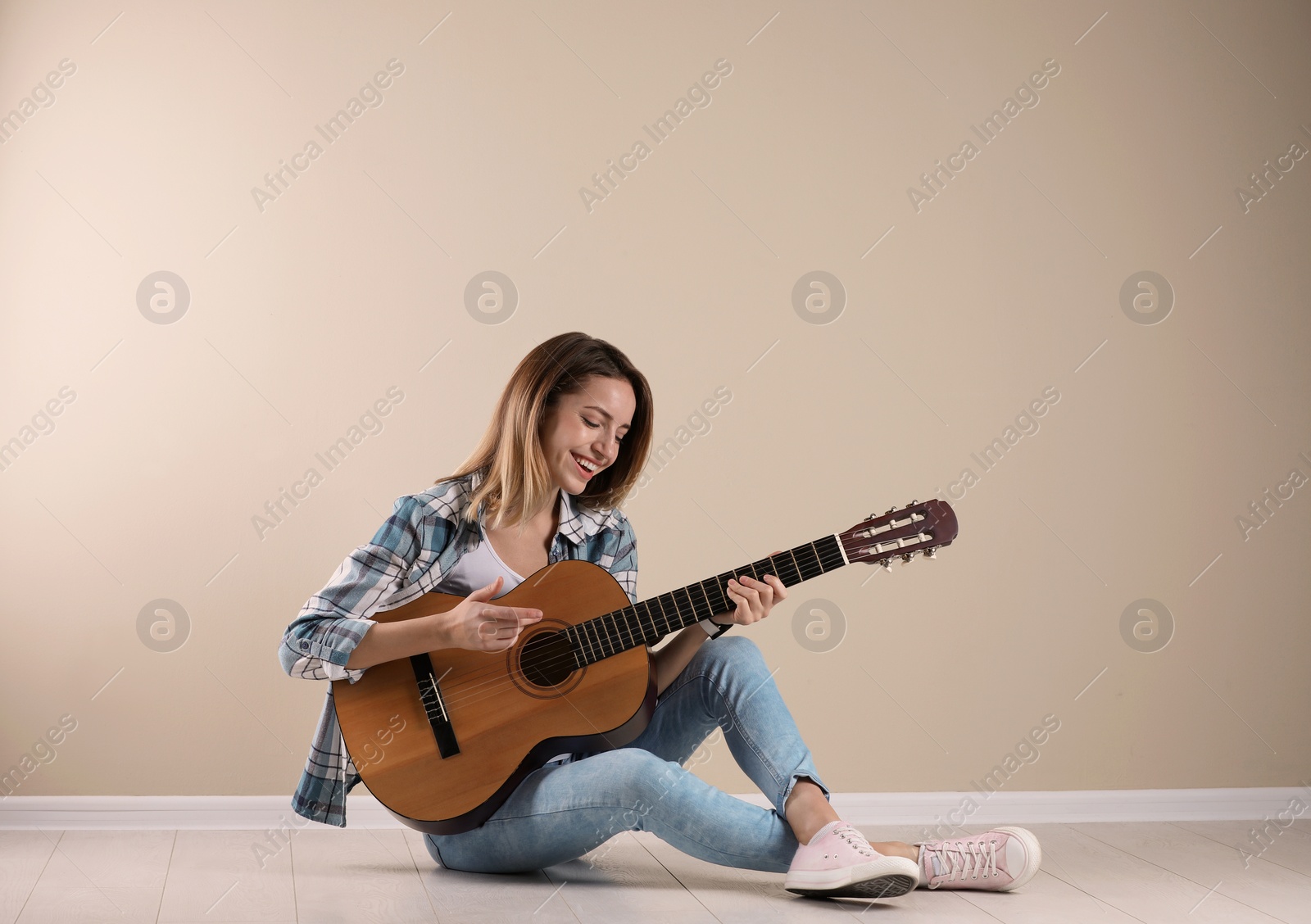 Photo of Young woman playing acoustic guitar near grey wall