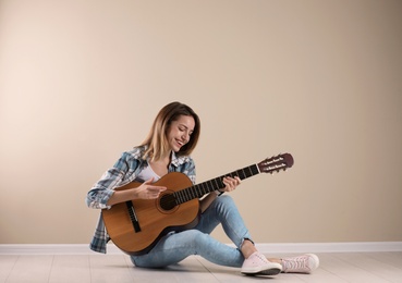 Photo of Young woman playing acoustic guitar near grey wall