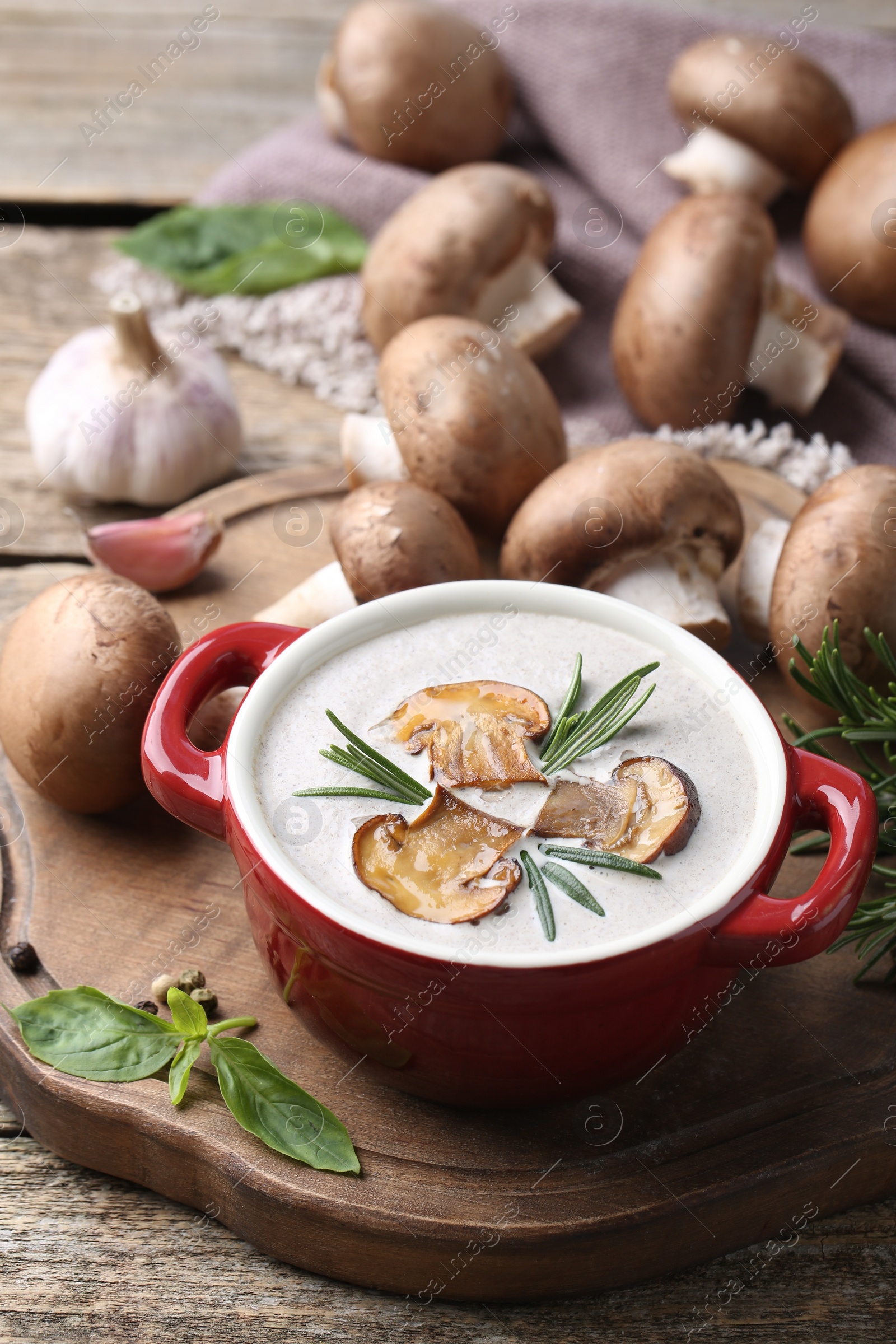 Photo of Delicious homemade mushroom soup in ceramic pot and fresh ingredients on wooden table