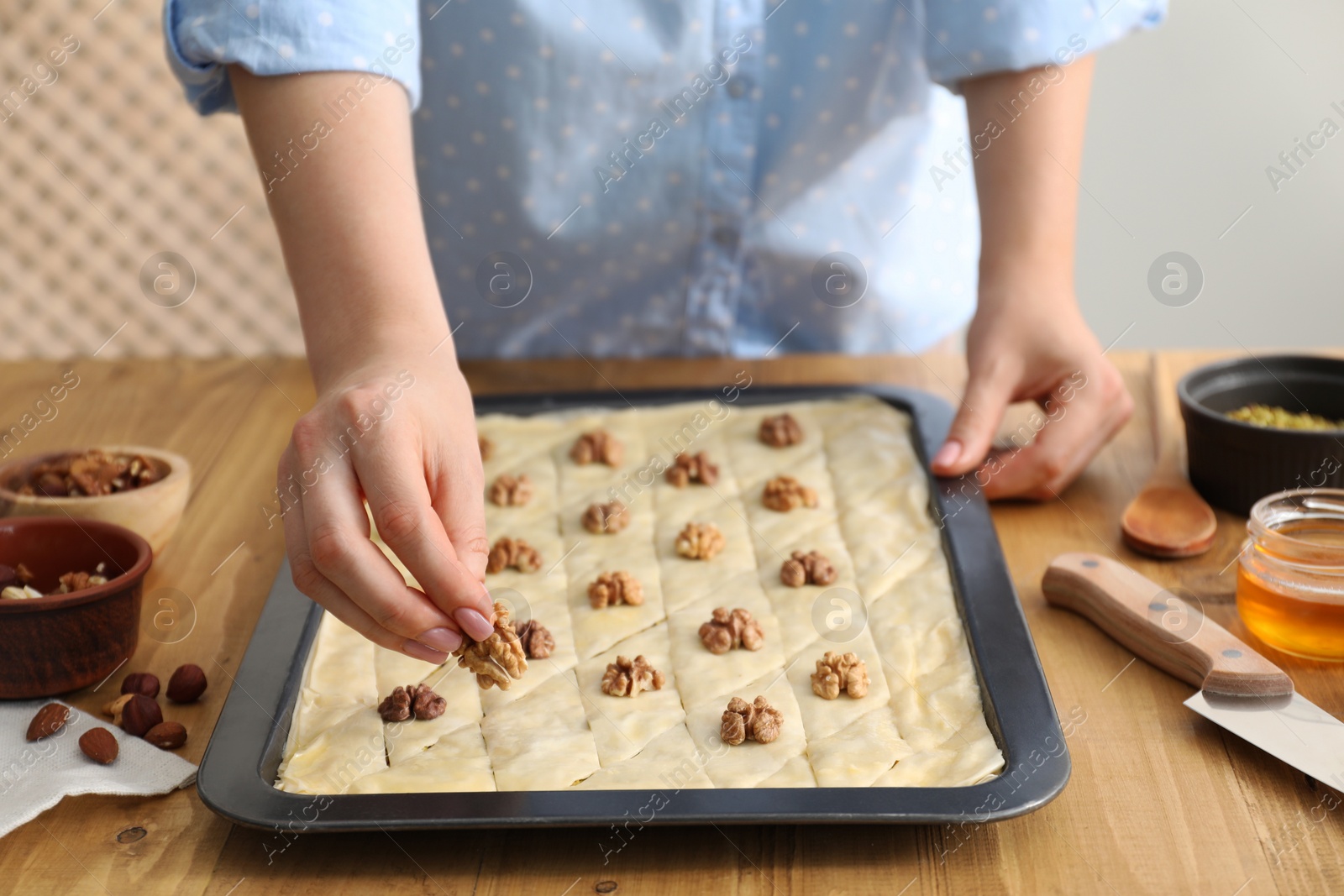 Photo of Making delicious baklava. Woman putting walnut onto dough at wooden table, closeup