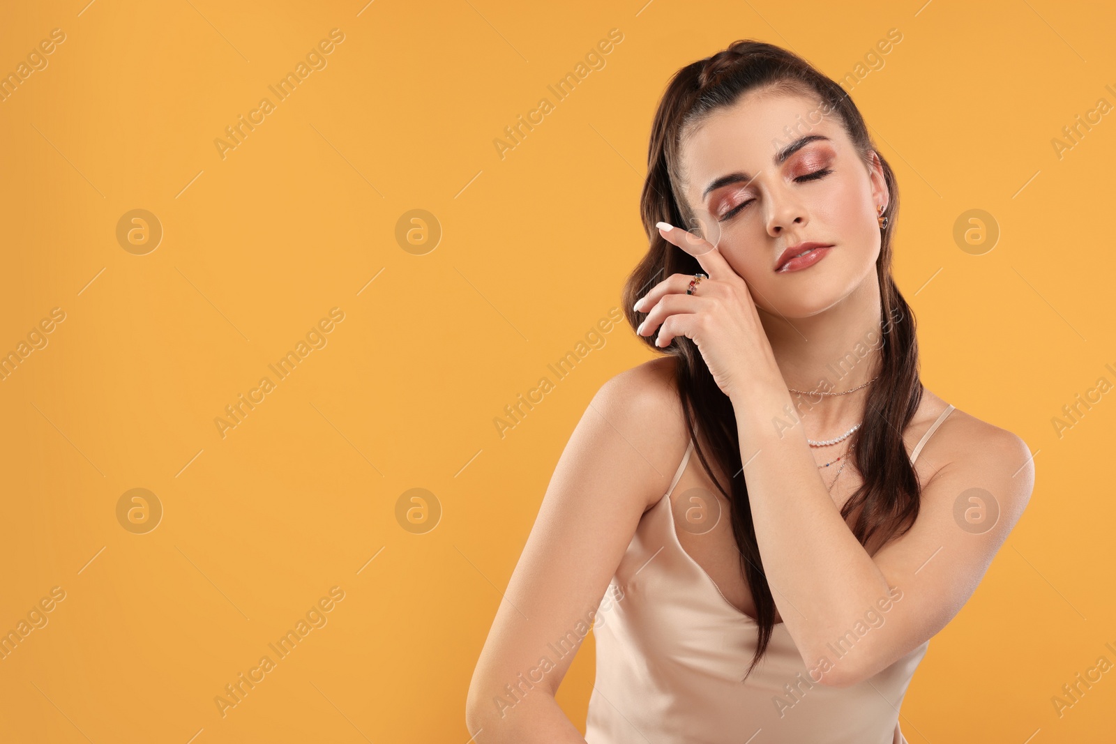 Photo of Beautiful woman with elegant jewelry on orange background, space for text