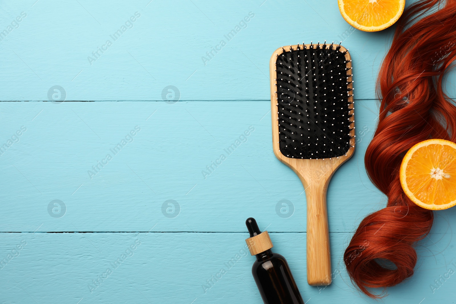 Photo of Brush, bottle of essential oil and red hair strand on light blue wooden table, flat lay. Space for text