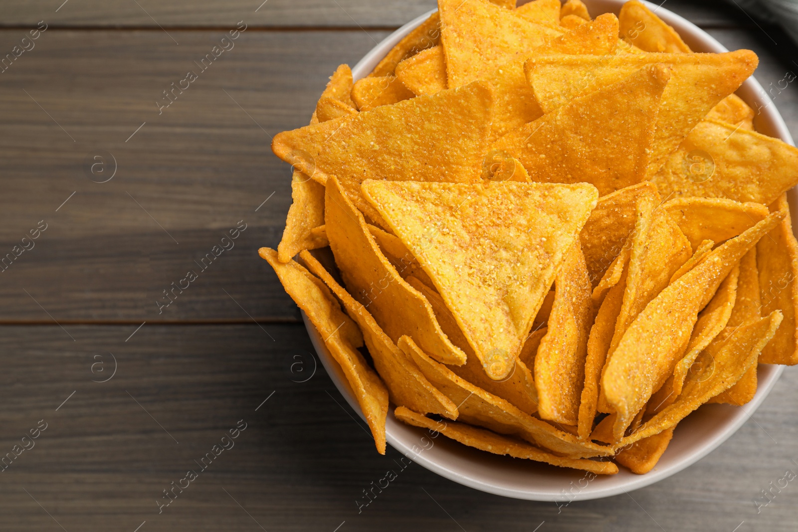 Photo of Tortilla chips (nachos) in bowl on wooden table, top view