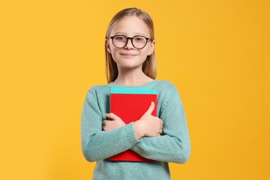 Photo of Portrait of cute girl in glasses with books on orange background
