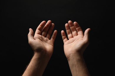 Photo of Religion. Man with open palms praying on black background, closeup