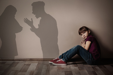 Image of Sad little girl sitting on floor indoors and silhouettes of arguing parents 