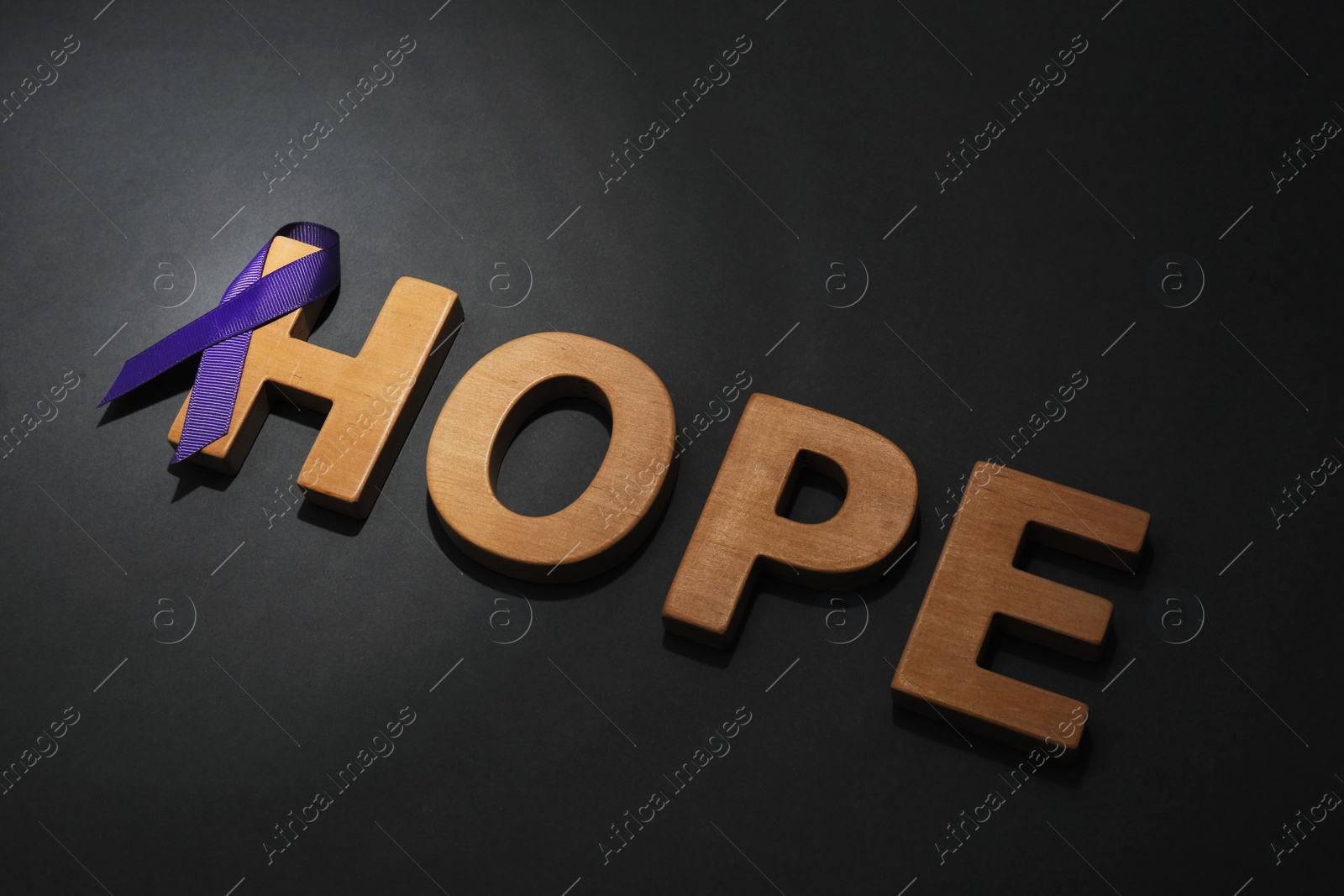 Photo of Purple awareness ribbon and word HOPE made of wooden letters on black background