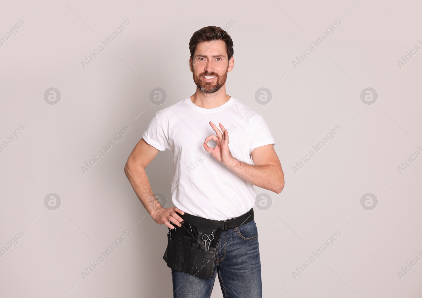 Photo of Smiling hairdresser with tool bag showing ok gesture on light grey background