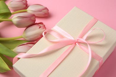 Photo of Beautiful gift box with bow and tulips on pink background, closeup