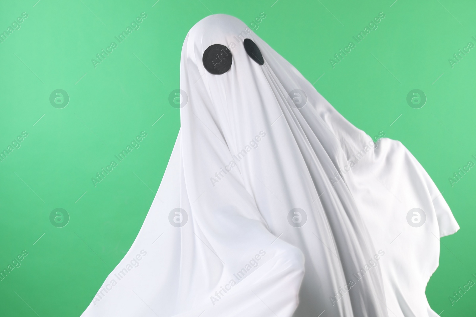 Photo of Creepy ghost. Person covered with white sheet on green background