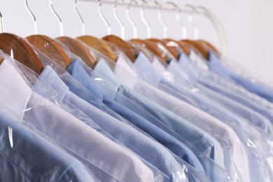 Photo of Hangers with shirts in dry cleaning plastic bags on rack against light background, closeup