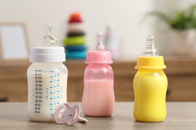 Photo of Feeding bottles with baby formula and pacifier on wooden table indoors